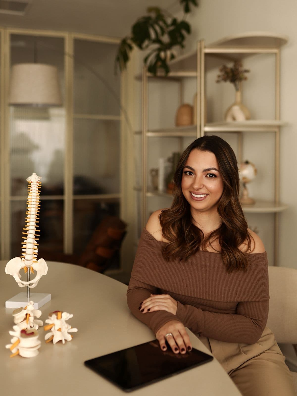 Profissional de quiropraxia em consultório com modelos de coluna sobre a mesa